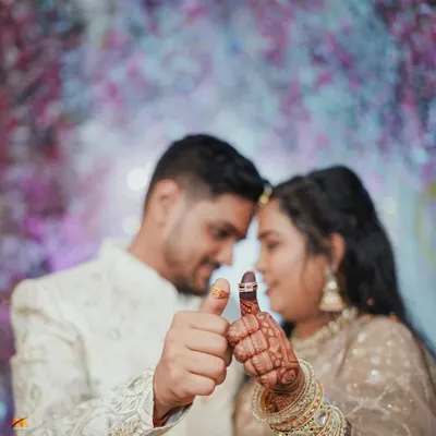 A creative engagement ring shot where the couple shows off their new rings on their thumbs. The focus is on the rings and their hands, with their happy faces blurred softly in the background.