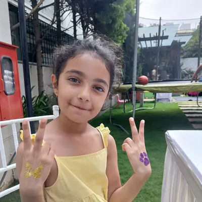 Double the fun with two glitter tattoos. This happy guest is showing off a golden butterfly on one hand and a purple paw print on the other, ready for a fun-filled party.
