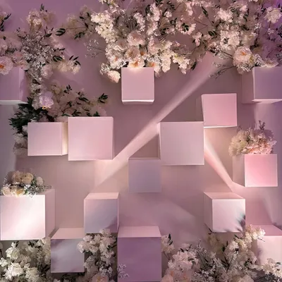 An all-white photo backdrop for a chic reception. The geometric cubes and delicate white blossoms create a modern, artistic, and utterly elegant setting. 🤍