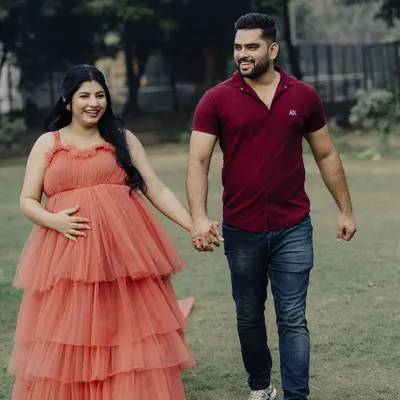 A happy couple during their maternity shoot. The mom-to-be looks radiant in our tiered coral gown, holding hands with her partner.