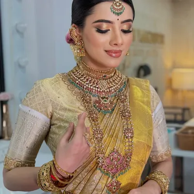 A breathtaking Muhurtham look in a golden Kanjeevaram saree. The makeup features a warm, glowing complexion, classic gold eyeshadow, and a perfectly defined lip, complemented by heavy temple jewelry for a regal finish.