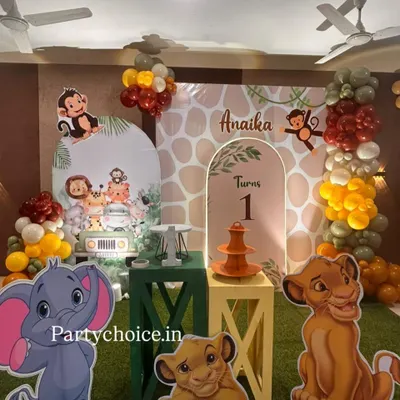 A complete jungle theme setup for a first birthday, featuring beloved characters from The Lion King and other animal friends. The decor includes a personalized backdrop, themed plinths, and character standees.