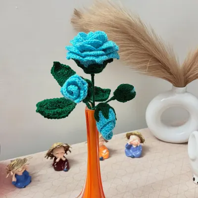 A handcrafted crochet blue rose stem with multiple flowers and buds, placed in a vase to show how it can enhance your home decor.