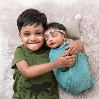 A proud big brother gives his newborn sibling a happy, toothy grin and a gentle hug. This shot perfectly captures the joy and excitement of a growing family.