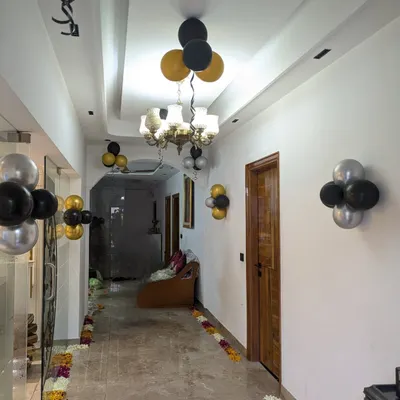 Hallway decoration for a party, using elegant clusters of black, gold, and silver balloons on the walls and ceiling to guide guests.