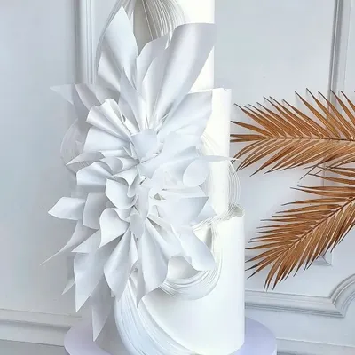 A breathtaking all-white, three-tiered wedding cake. This modern masterpiece features abstract, sculptural white chocolate decorations, creating a look of pure elegance and sophistication.