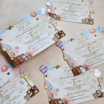 A whimsical travel-themed baby shower invitation. We used custom illustrations of hot air balloons, suitcases, and airplanes with a die-cut cloud border to create a sense of adventure for the new arrival.