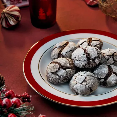 A cozy Christmas scene featuring chocolate crinkle cookies for Marriott Bonvoy. The warm lighting from the candle and the rich red tones of the plate and decor create a classic, festive atmosphere.