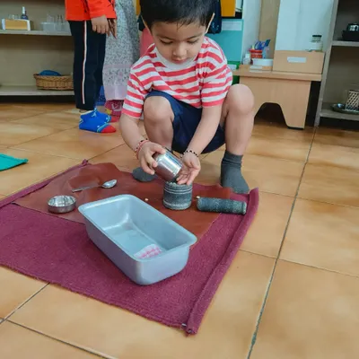 A child carefully pouring from one container to another. This simple activity is a lesson in precision, control, and concentration, building skills that are essential for writing and other academic work.