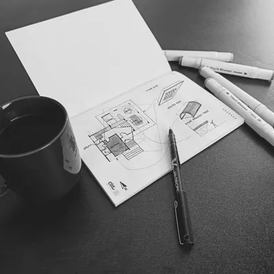 The beginning of a new project often looks like this: a sketchbook, a pen, and a cup of coffee. Here, I am exploring initial ideas for a farmhouse, translating thoughts into hand-drawn possibilities.