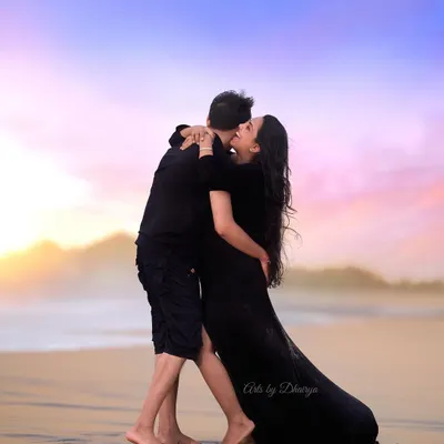 An expressive kiss shared at the water's edge during a Goa maternity shoot. The rich colors of the sunset sky and the dark silhouettes create a powerful and romantic image.