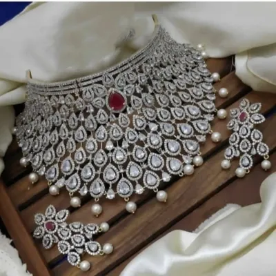 This grand choker set is designed to make a statement. The intricate web of diamond-look stones with a central ruby-red stone and pearl drops is perfect for a reception lehenga or gown.