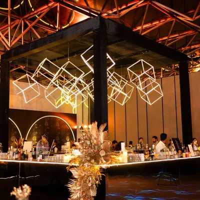 A modern, industrial-themed sangeet featuring a spectacular installation of glowing geometric cubes suspended over the main bar. The black and gold palette adds a layer of sophisticated glamour.