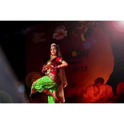 A Bharatanatyam dancer is captured mid-performance on stage, with a dramatic lens flare adding to the energy. My technical setup with a Nikon Z6 and Godox lighting ensures crisp images even in challenging, fast-paced stage environments.
