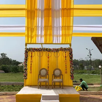 A classic outdoor Haldi stage setup. I used bright yellow and white drapes for the canopy, with a floral-framed yellow backdrop and traditional chairs for the ceremony.
