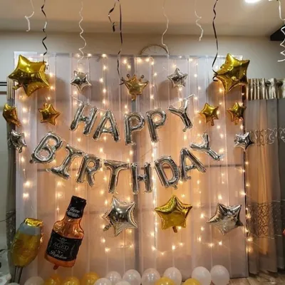 A perfect setup for an adult birthday party, featuring a backdrop of warm fairy lights. The decoration is accented with silver and gold star-shaped balloons and a fun whiskey bottle foil balloon.