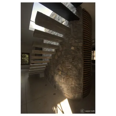 The central feature of the apartment is this sculptural staircase, with concrete cantilever steps emerging from a curved random rubble wall, leading up to a skylight.