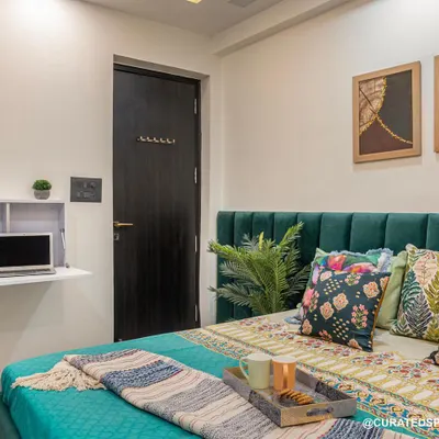 This beautiful emerald green bedroom was designed with functionality in mind. It features a fold-down study desk, perfect for small spaces, and a comfortable bed with vibrant, patterned cushions.