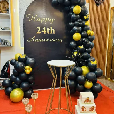I also provide decorations for anniversaries, like this elegant setup for a 24th anniversary. The black backdrop with gold lettering is framed by a black and gold balloon arch, creating a sophisticated and celebratory look.