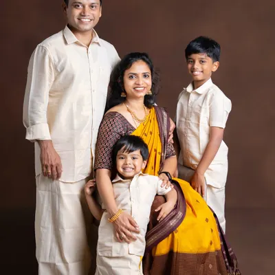A beautiful family of four dressed in coordinated traditional outfits. The mother's yellow saree and the father and sons' matching veshtis create a vibrant and classic portrait.