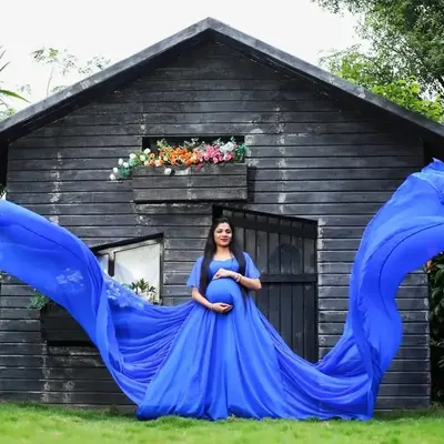 A vibrant royal blue gown with a long, flying trail creates a breathtaking image against a rustic outdoor backdrop. This is a perfect example of a high-impact outdoor maternity portrait.