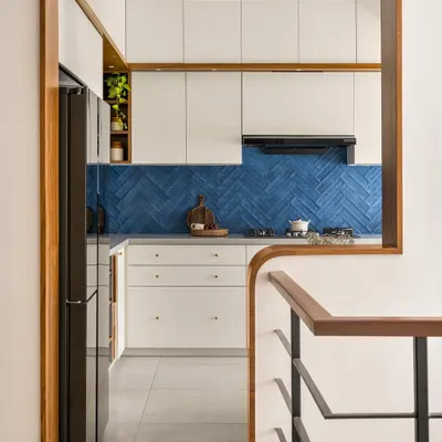 In our 'Palaash' project, we used a bold blue herringbone tile backsplash to create a stunning focal point. The kitchen is viewed through a custom wood-framed arch, connecting it beautifully to the rest of the home.