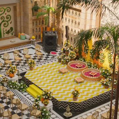 An aerial view of a vibrant Haldi setup in an inner courtyard, featuring a modern yellow and white chevron stage floor. This shows how I blend contemporary patterns with traditional ceremony spaces.