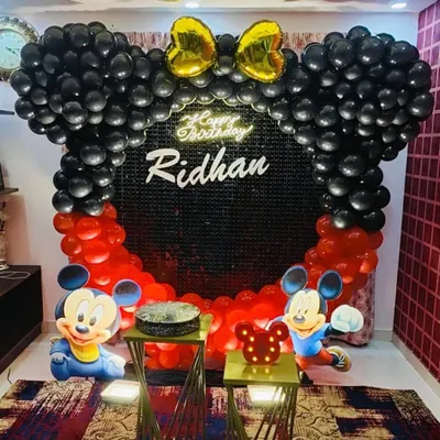 A classic Mickey Mouse themed birthday setup with a black sequin backdrop and a balloon arch shaped like Mickey ears.