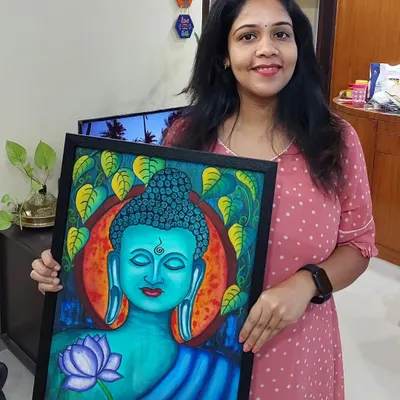 Here I am, holding a finished Buddha painting with a vibrant blue and orange background. The Bodhi leaves and lotus flower add to the serene feeling.