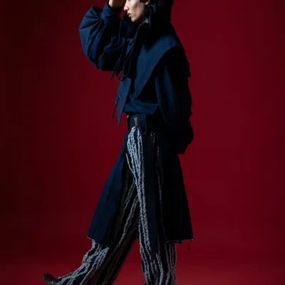 A high-contrast fashion story. The clash of the bold red background with the deep blue, avant-garde outfit creates a visually arresting image.