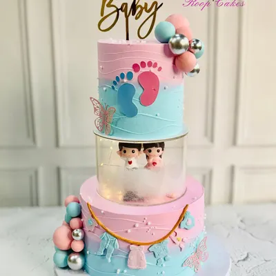 Sweet beginnings and a little bundle of joy on the way. This grand three-tier baby shower cake features pink and blue ombre, tiny fondant clothes, and cute baby figurines peeking out from the middle tier.