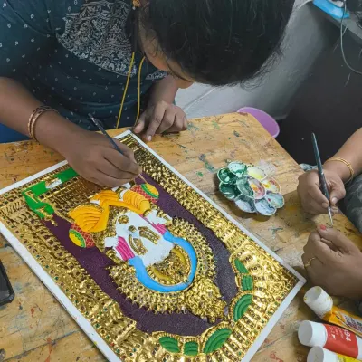 A student carefully applies gold leaf to a Tanjore painting. This traditional art form requires immense patience and precision, skills that are valuable for any aspiring artist.