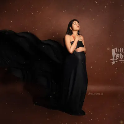 A dramatic solo portrait featuring a flowing black satin gown against a rich, textured backdrop. The movement of the fabric adds a powerful and artistic element to this glamorous maternity photo.