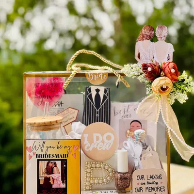 This "Will you be my bridesmaid?" proposal box is a beautiful way to ask your best friends to be part of your bride tribe. It's a transparent bag filled with personalized goodies like a custom wine glass, initial pin, and a photo card.