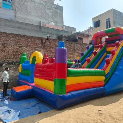 A new model of a large, colorful bouncy castle with multiple activity zones. A person is standing next to it, showing the impressive scale of the structure.