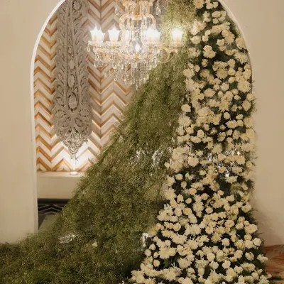 I create fairytale entrances that set the tone for the entire event. This stunning archway, overflowing with baby's breath and white roses, frames a view of a crystal chandelier, promising a night of elegance.