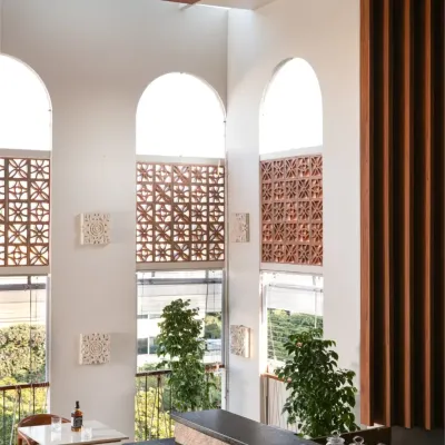 We transformed a bare concrete shell into a slice of Bali in the city. The double-height arched windows flood the space with sunlight, while handmade terracotta jalis and tropical plants bring an earthy, serene island soul to this urban cafe.