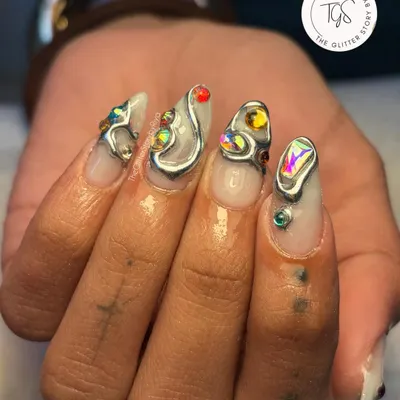 An edgy and artistic set featuring sculpted silver elements. Each nail has a unique abstract design, accented with colorful crystals for a pop of color against the metallic finish.