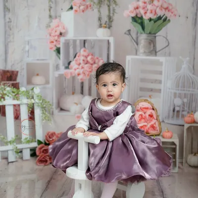 This little girl looks like a princess in her satin purple dress, posing on a white tricycle against a rustic floral backdrop.