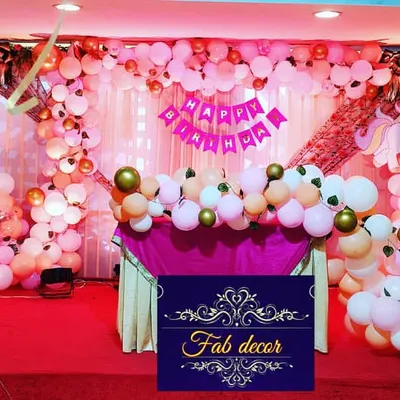 A full view of a unicorn-themed birthday stage I designed. The setup features a large balloon arrangement in pinks and golds, a decorated cake table, and unicorn character elements to bring the theme to life for a baby girl's party.
