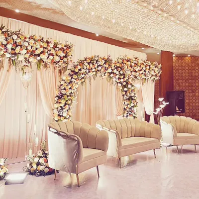 A classic and grand reception stage featuring lush floral arches in pastel shades, elegant drapery, and a magnificent crystal chandelier overhead. This timeless design exudes sophistication and romance for a perfect wedding celebration.