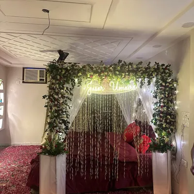 A dreamy 'Welcome Bride' setup with a four-poster bed decorated with flowers and a custom neon sign. The floor is covered in a sea of red rose petals, creating an incredibly romantic atmosphere.