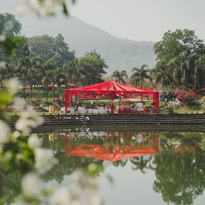 Set against a serene lake, the vibrant red canopy of the La Tomatina Haldi creates a stunning contrast with the natural landscape. This view captures the scale and boldness of the concept.