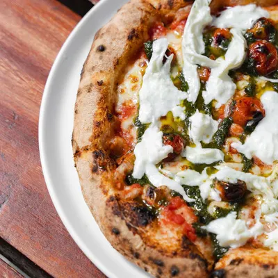 Our Stracciatella Pizza is a study in freshness. It features vibrant confit cherry tomatoes and a drizzle of homemade pesto, perfectly complemented by creamy, hand-torn stracciatella cheese.