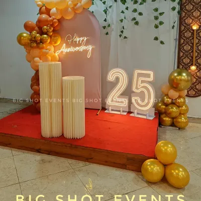 Celebrating a silver jubilee, this 25th-anniversary decor features large marquee numbers, a neon sign, and a beautiful balloon arrangement on a raised stage.