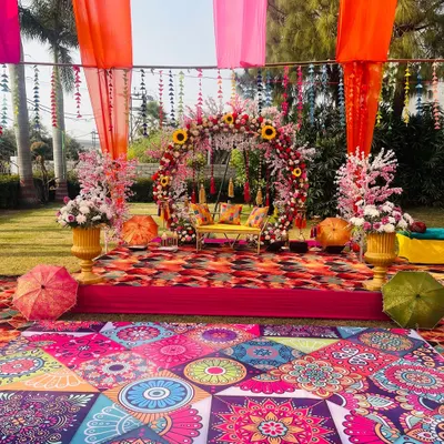 A vibrant Haldi and Mehendi stage setup with a beautiful floral swing. The colorful printed flooring and bright drapes create a festive atmosphere perfect for an outdoor celebration.