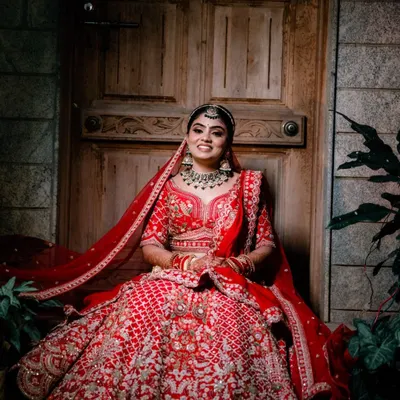 A breathtaking bridal portrait. This bride looks absolutely radiant in her red lehenga, seated in a way that showcases the grandeur of her outfit.