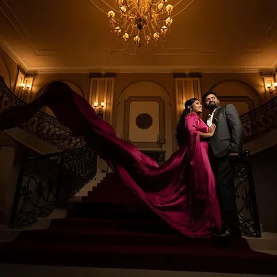 A low-angle shot emphasizing the grandeur of a palatial staircase, with the couple in formal wear and her magenta gown creating a dramatic, fairy-tale scene.