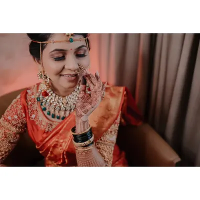 A close-up bridal portrait capturing the bride's gentle smile as she adjusts her nath (nose ring), a classic element of Maharashtrian bridal jewelry.