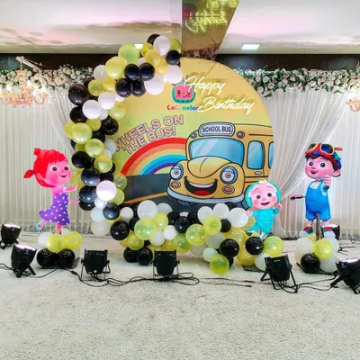 A fun Cocomelon-themed birthday party setup for a young child. I created a custom circular backdrop with characters from the show, framed by a balloon arch in a yellow, black, and white color scheme.